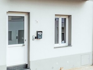 A white building with a door and a window, a mailbox, and a small vent on the wall.