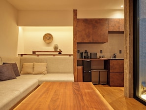 Ein modernes Wohnzimmer mit Couch, Küchenzeile, Kühlschrank und Schränken sowie einem Holztisch.