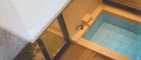Esquina de una habitación con una terraza de madera y una pequeña piscina con borde de azulejos.