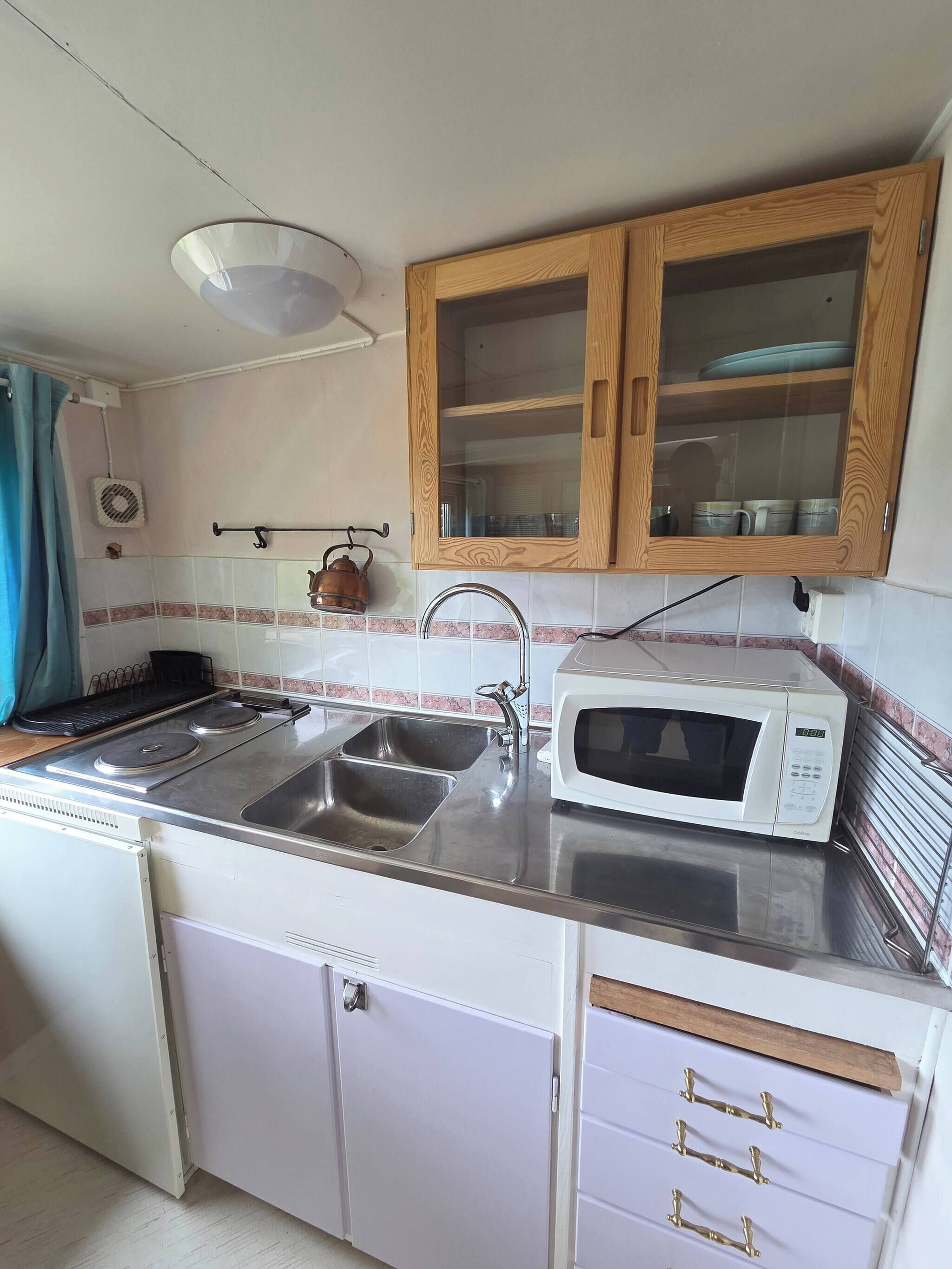 A compact kitchen with a sink, stove, microwave, and wooden cabinets.