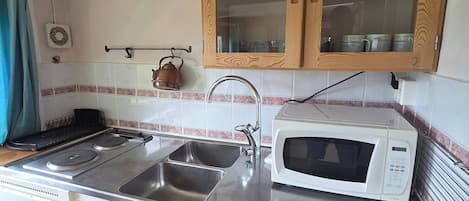 Een kleine keuken met een spoelbak, fornuis, magnetron en houten kastjes.