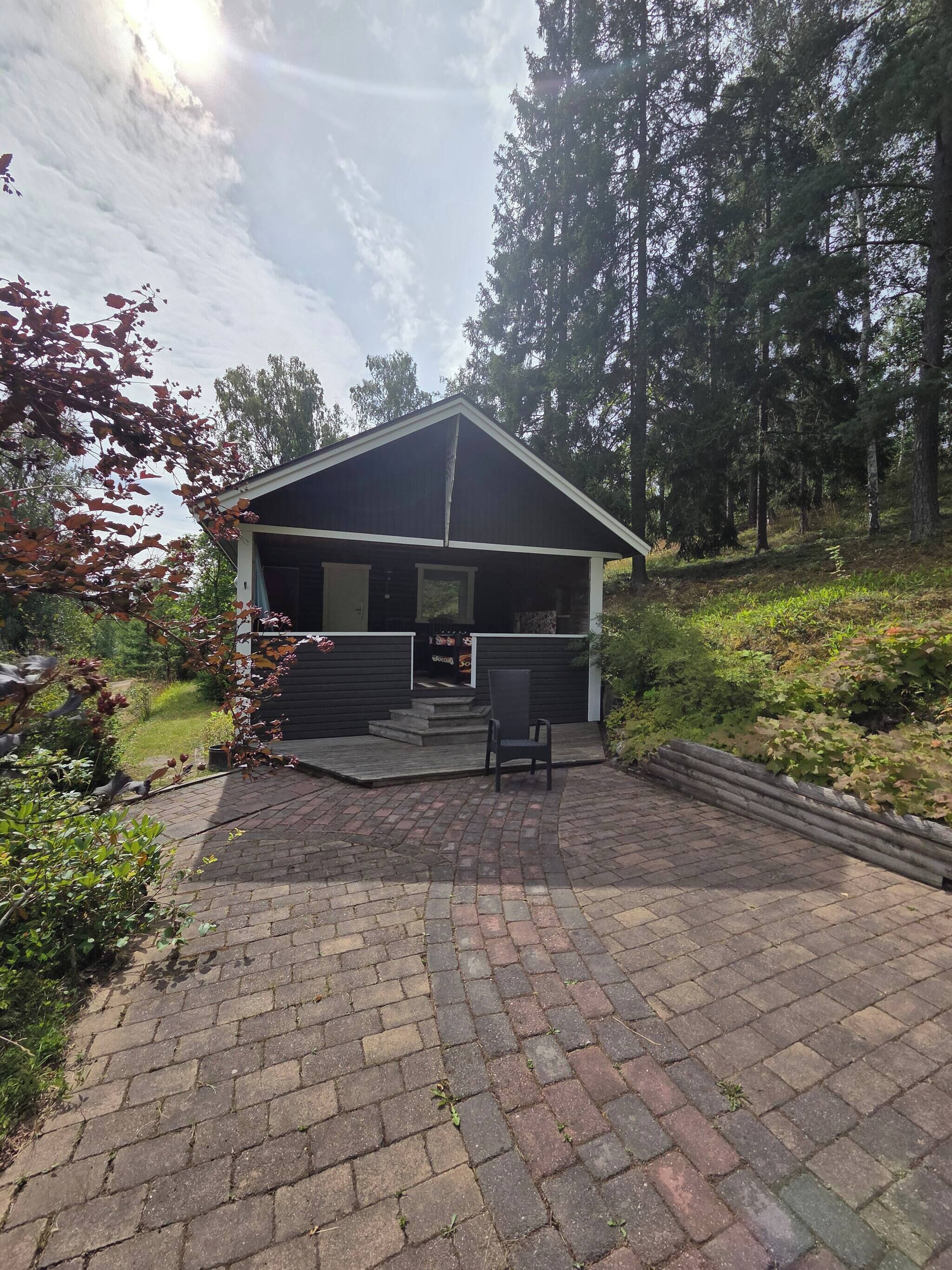 A wooden cabin with a porch, surrounded by trees and a brick patio.