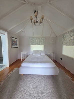 Une chambre à coucher avec un grand lit, un lustre, une fenêtre ornée d’un rideau à motifs d’arbres et une porte.
