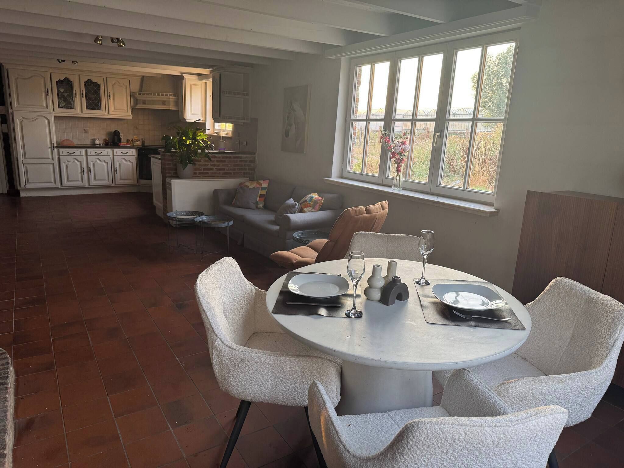 A dining area with a round table set for two, a sofa, and a kitchen in the background.
