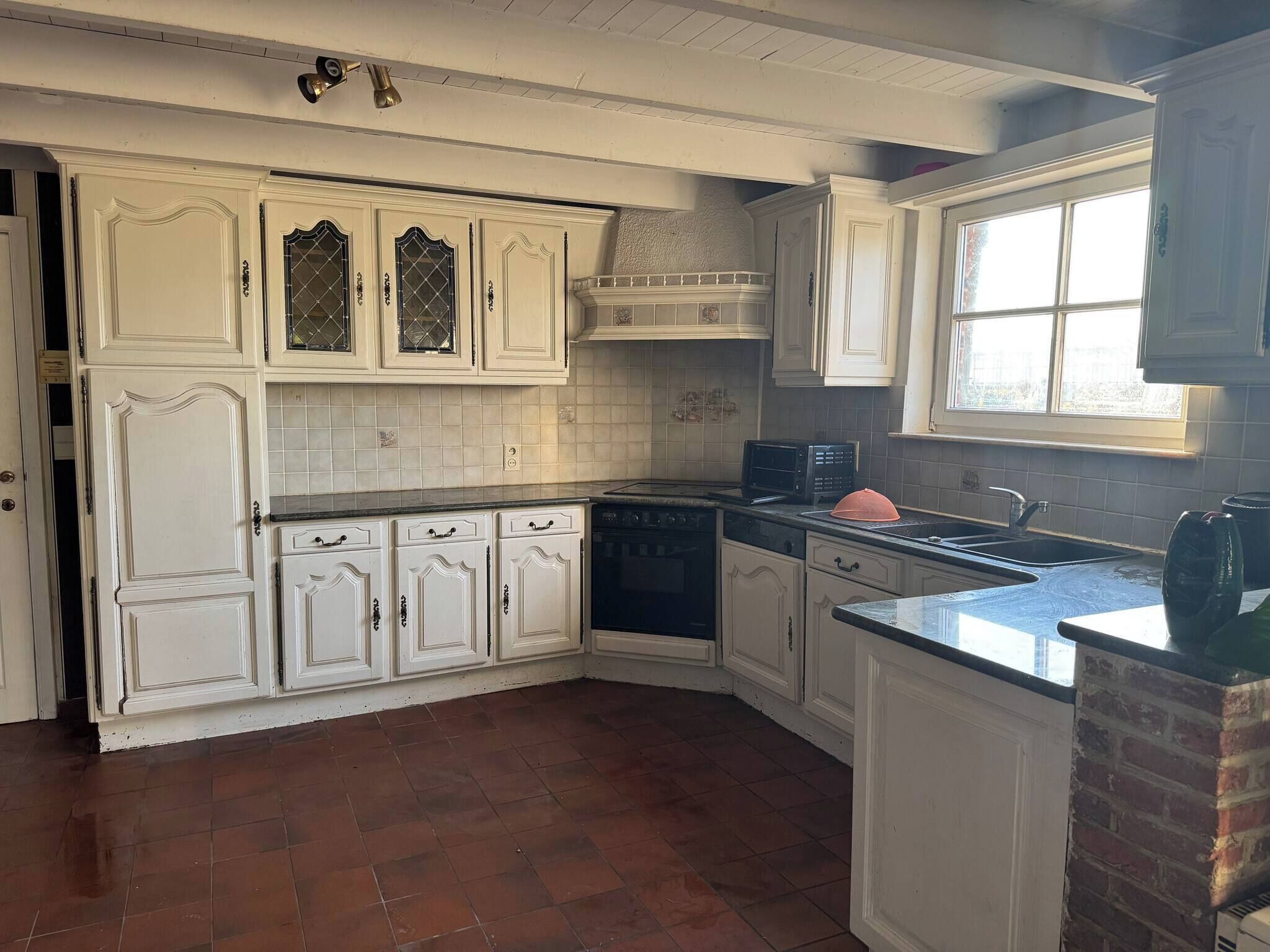 Cocina con muebles blancos, estufa y ventana.