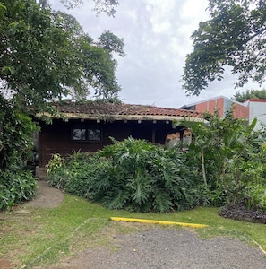 A rustic building with a tiled roof, surrounded by lush greenery and a paved pathway. - Peaceful Garden Guest House — 5 Minutes from SJO Airport (La Ribera de Belen)
