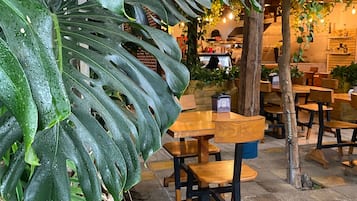 An indoor dining area with wooden tables and chairs, surrounded by large tropical plants and hanging plants.