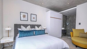 Ein modernes Schlafzimmer mit einem großen Bett, Nachttischen, einem Sessel und einem durch eine offene Tür einsehbaren Badezimmer.