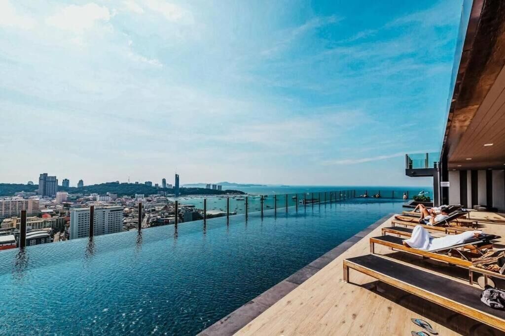 An infinity pool with a city view, lounge chairs, and a wooden deck.