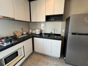 A kitchen with white cabinets, a black countertop, a built-in oven, a stainless steel refrigerator, and a shelf with glasses. - 2 Bed Room Sea View Great Place Central (Muang Pattaya)