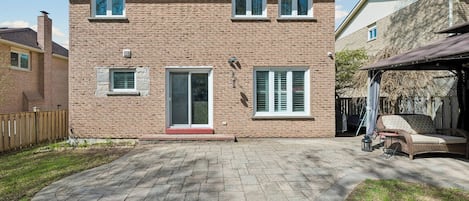 Una casa de ladrillo de dos pisos con un porche cubierto, una puerta principal y un ventanal lateral pequeño.