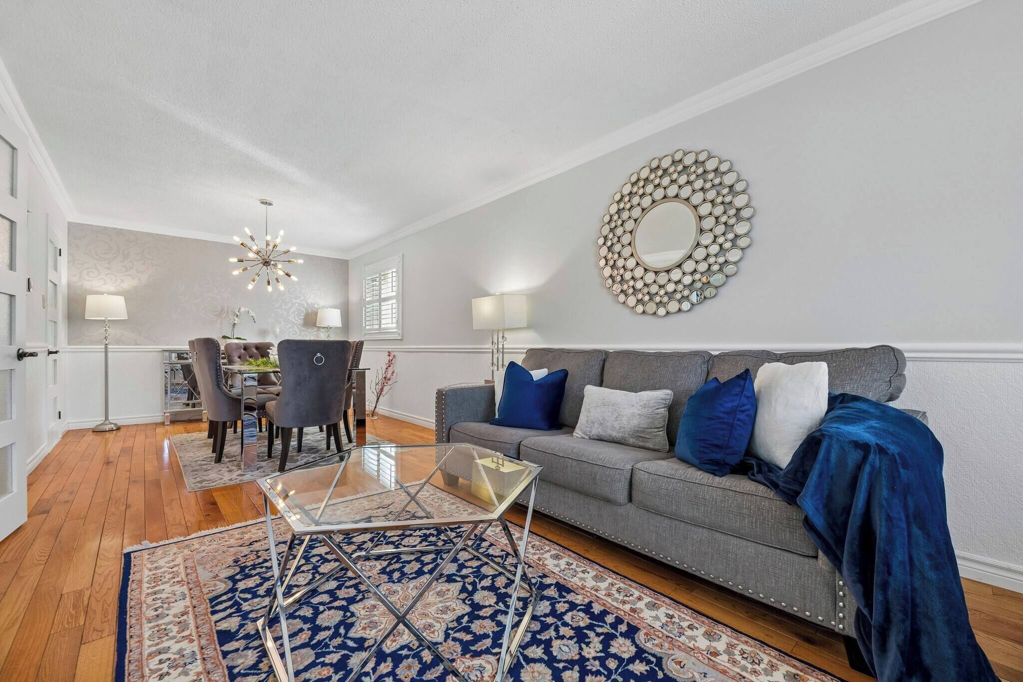 A living room with a grey sofa, blue and white cushions, a glass coffee table, and a patterned rug.