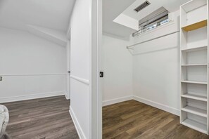 A walk-in closet with white walls, wooden flooring, and a ceiling vent.