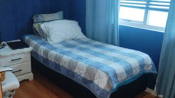 A bedroom with a bed, a dresser, a chair, and a window with curtains.