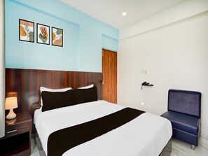 Ein Hotelzimmer mit einem Bett, einem Nachttisch, einer Lampe, einem Sessel und drei gerahmten Kunstwerken an der Wand.