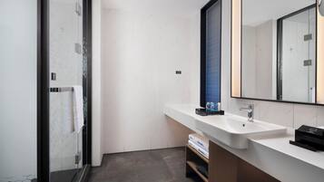 Un baño moderno con un lavamanos blanco, un espejo grande y una zona de ducha.