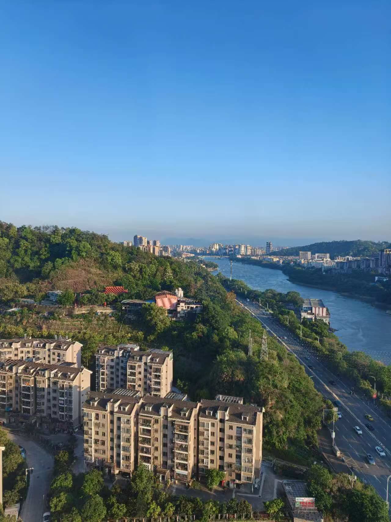 A high-rise residential building with multiple balconies, a river in the background, and a clear sky.