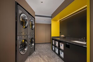 A modern laundry room with stacked washers and dryers, a large mirror, and a sink with storage baskets. - Hampton by Hilton Fuzhou Software Park (Fuzhou)