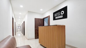 Uma área de recepção de hotel com balcão, painel de parede em madeira e sinalização indicando serviço corporativo.