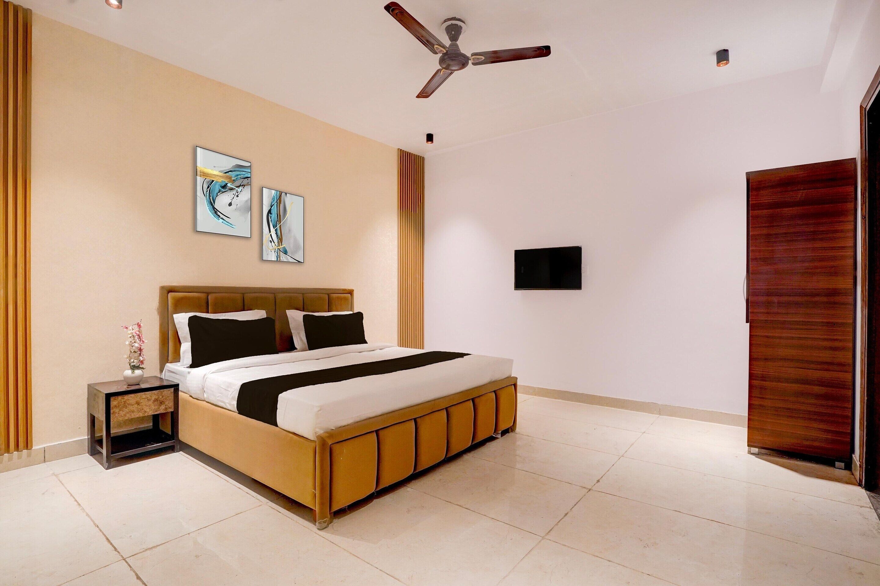 A bedroom with a bed, a nightstand, a ceiling fan, artwork on the wall, and a door.