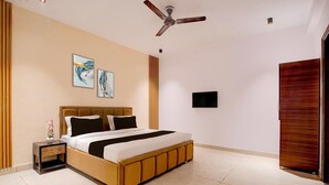 Um quarto com uma cama, uma mesinha de cabeceira, um ventilador de teto, obras de arte na parede e uma porta.