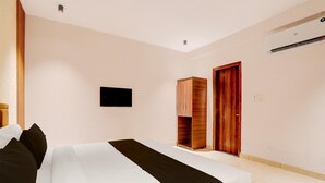 Quarto de hotel com cama, guarda-roupa, televisão e ar condicionado.