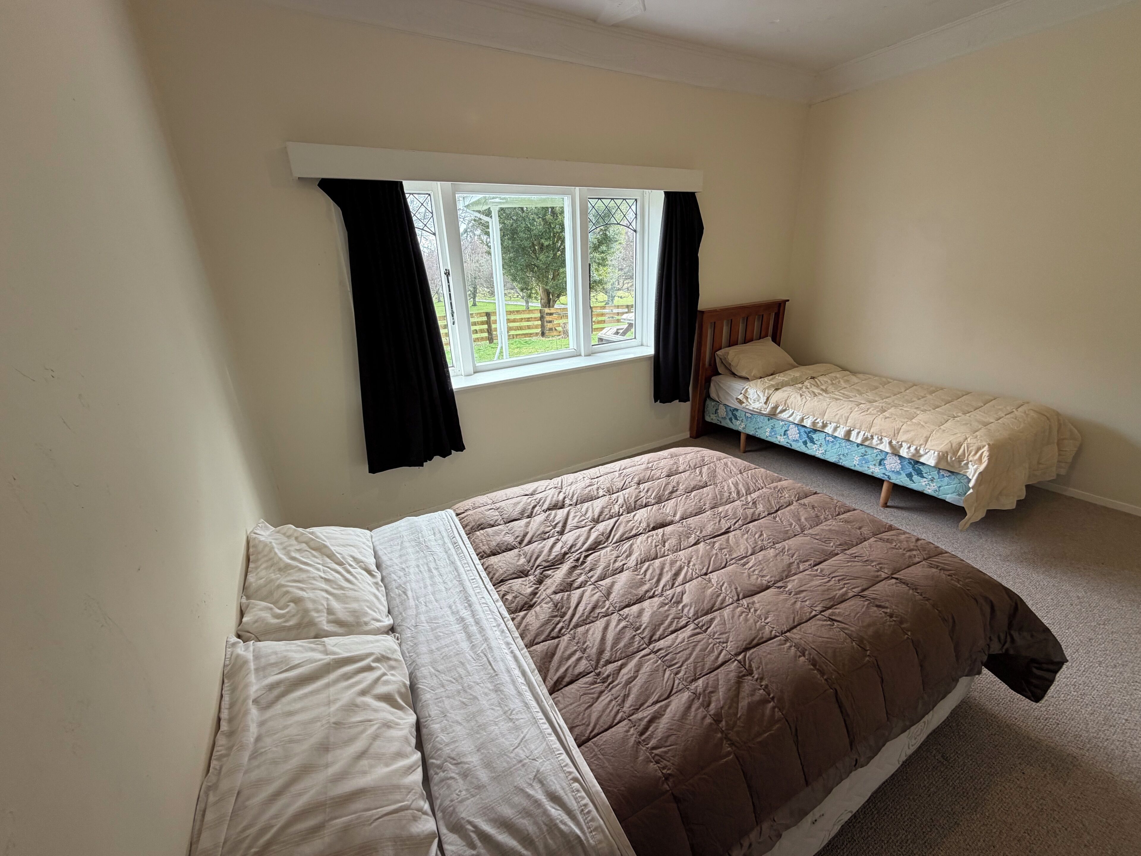 Ein Schlafzimmer mit zwei Betten, einem Fenster mit Vorhängen und Blick auf Grünflächen.
