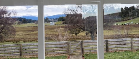 A covered porch with a view of a rural landscape, including fields and a distant mountain range.