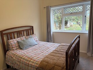 A bedroom with a wooden bed, a window with curtains, and a view of greenery outside.