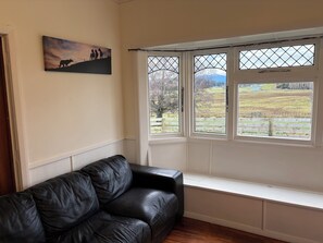 Una habitación con un sofá de cuero negro, un cuadro en la pared y una ventana con vista a un campo y árboles.