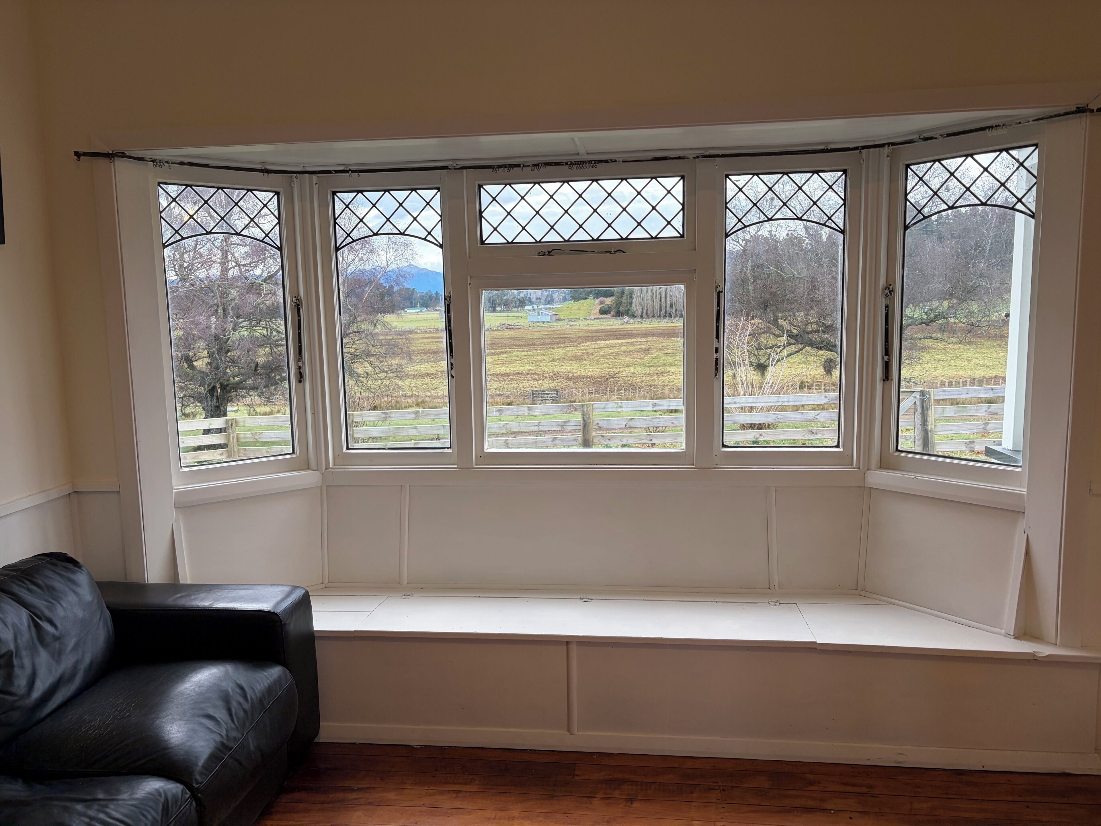A room with a bay window overlooking a rural landscape.