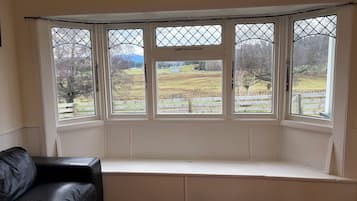 A room with a bay window overlooking a rural landscape.