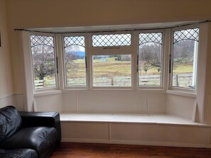 A room with a bay window overlooking a rural landscape.