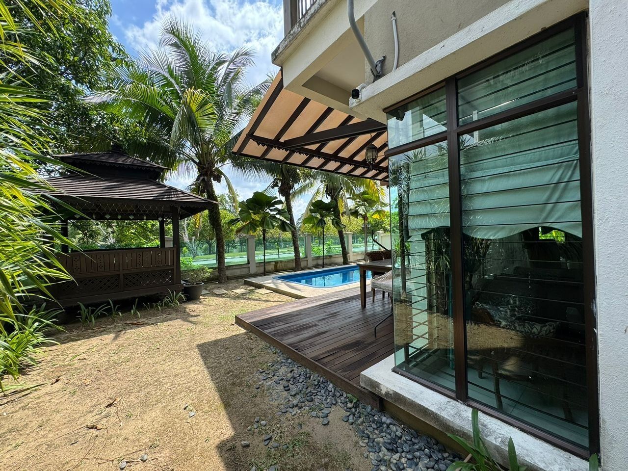 A modern outdoor area with a wooden deck, a swimming pool, and a covered seating area.