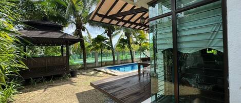 A modern outdoor area with a wooden deck, a swimming pool, and a covered seating area.