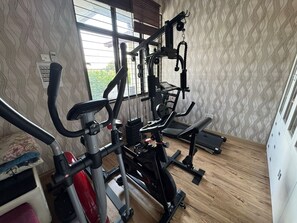 A gym with exercise equipment, a window with blinds, and patterned wallpaper.