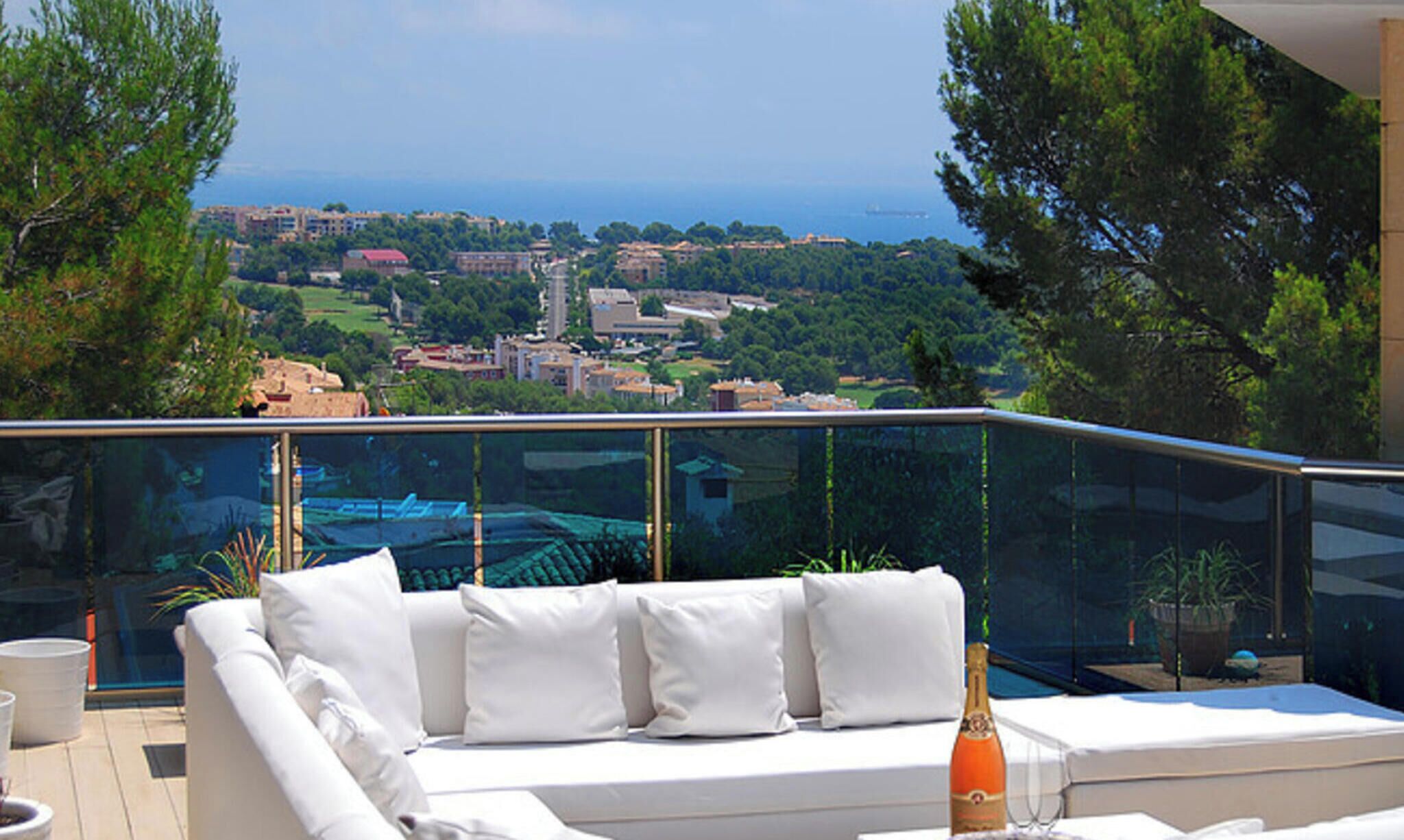 Un balcon avec un canapé blanc, une balustrade en verre et une vue sur une ville côtière.