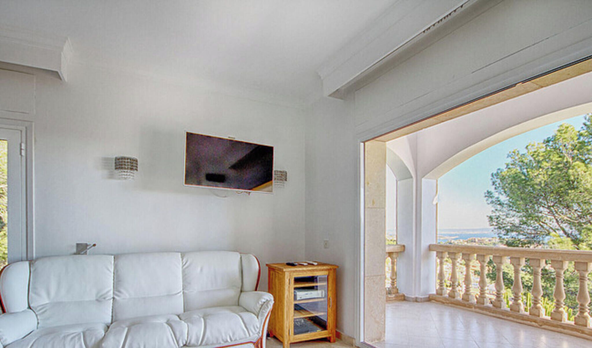 Ein weißes Sofa, ein an der Wand befestigter Fernseher und eine Holzkommode mit Regalen.