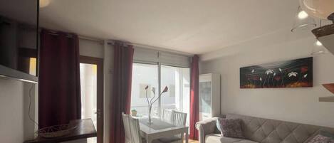 A living room with a sofa, a dining table with chairs, and a painting on the wall.