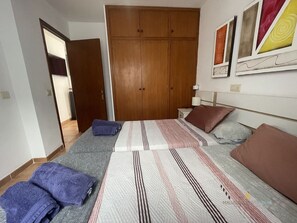 Ein Schlafzimmer mit Bett, Kissen, einem Nachttisch, einem Kleiderschrank und einer Tür zu einem anderen Raum.