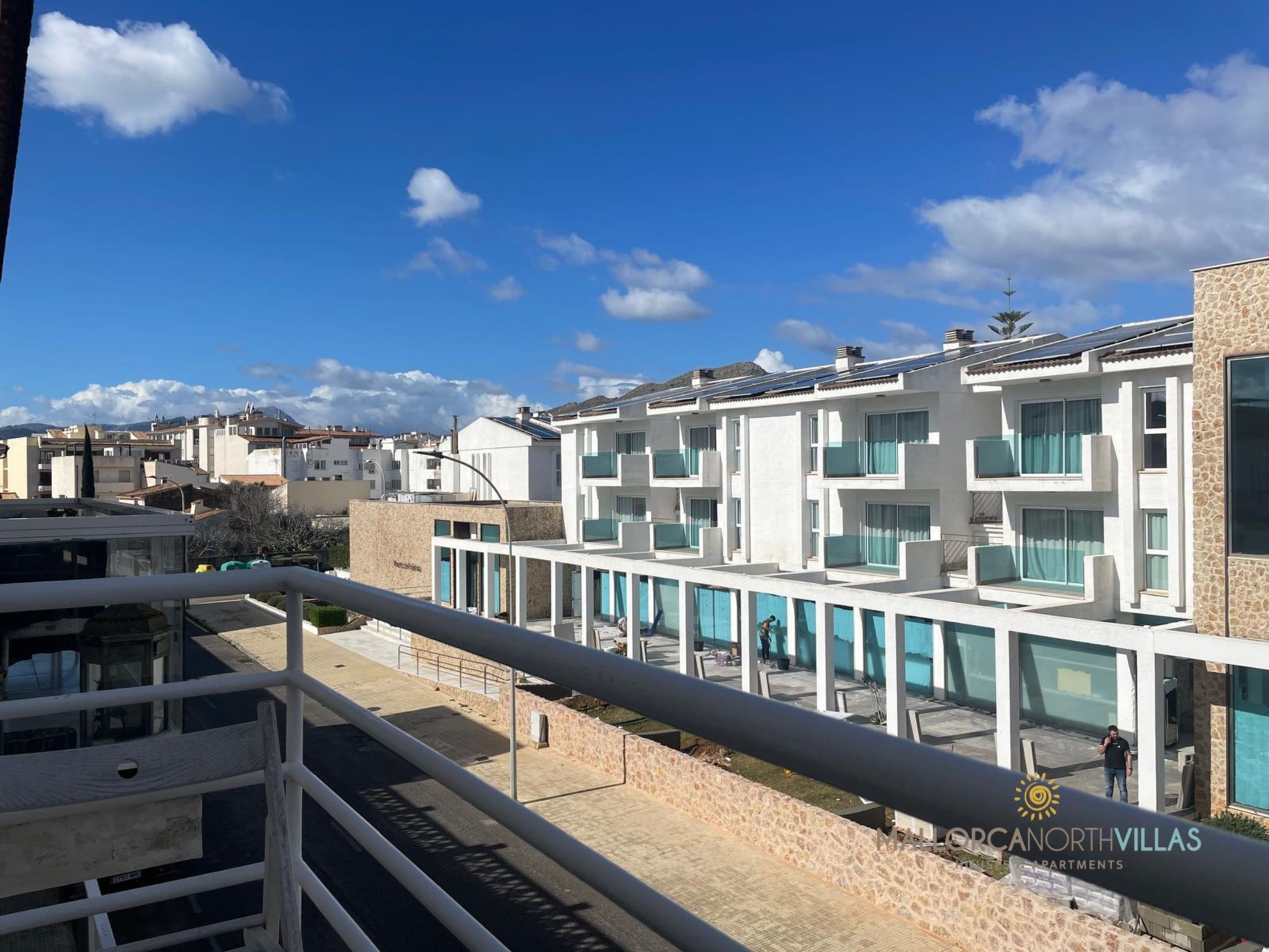 A modern apartment complex with multiple balconies, a clear sky, and a view of the surrounding neighborhood.
