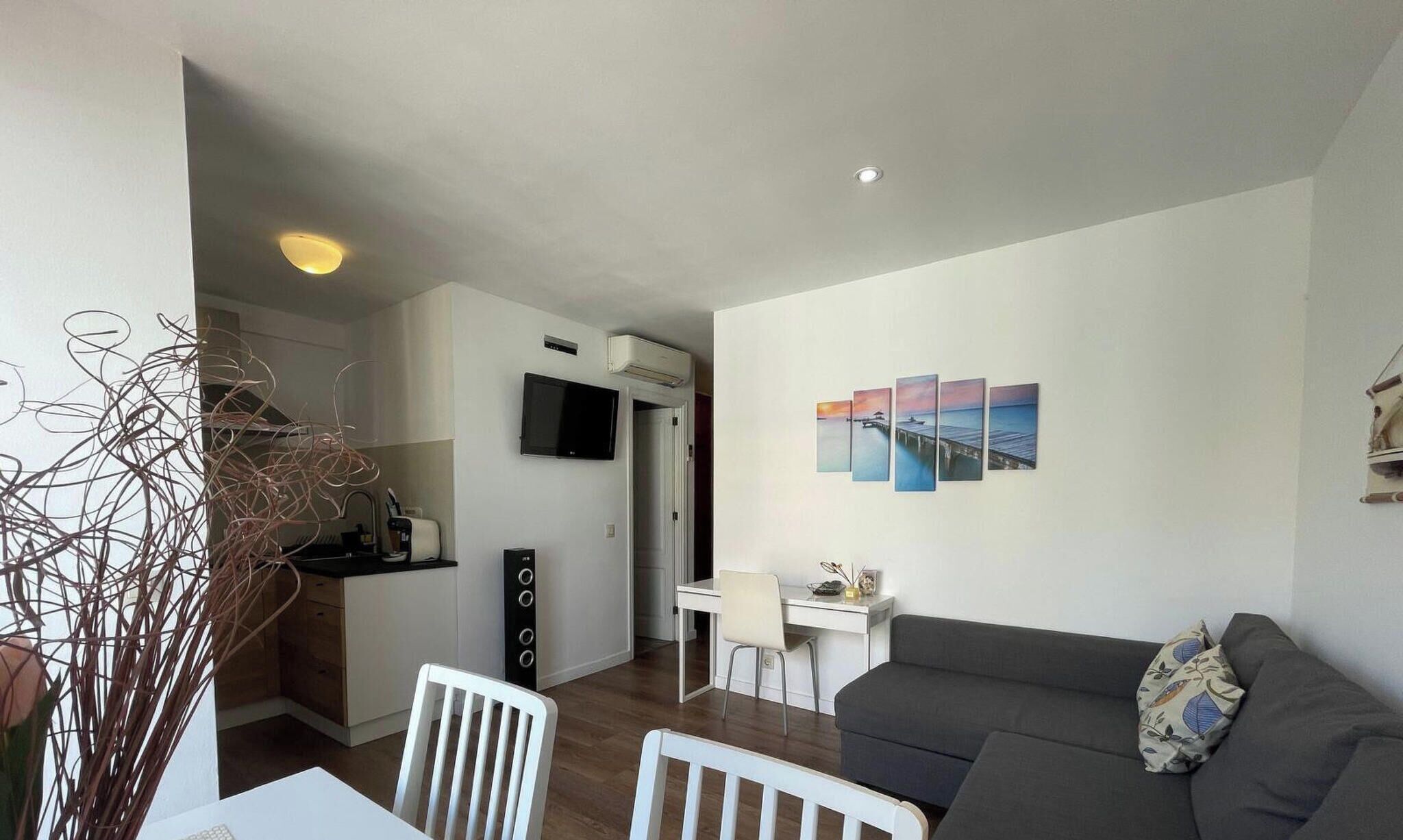 Ein modernes Wohnzimmer mit einer Couch, einem Esstisch mit Stühlen, einer Küchenzeile mit Fernseher und einer Wand mit einer Reihe von Gemälden.
