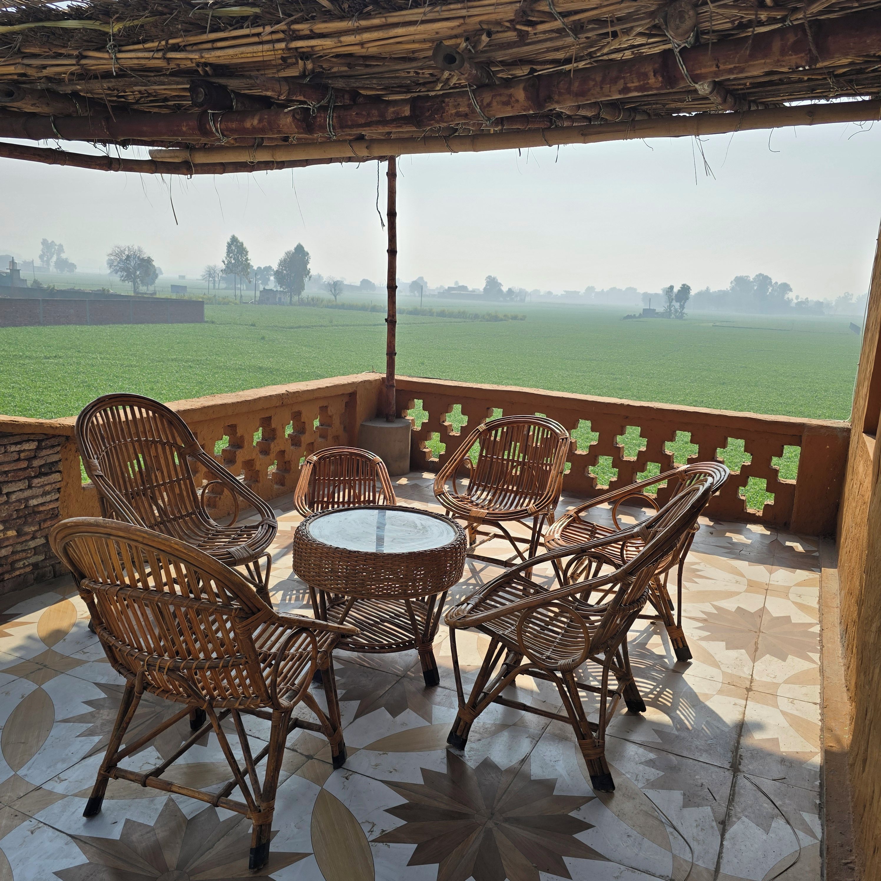 A covered outdoor seating area with wicker furniture and a view of a green field.