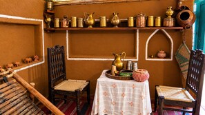 A traditional room with a woven chair, a small table with a tray, and a shelf with metal containers.