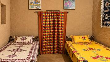 A bedroom with two beds, a ceiling fan, and two wall-mounted paintings.