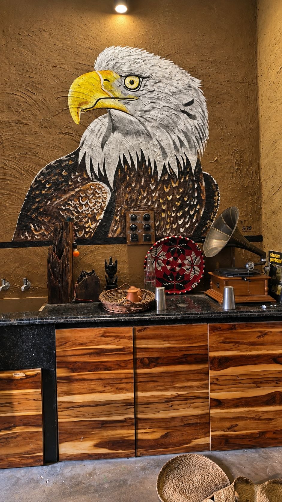 A bar area with a large eagle mural, wooden cabinets, and various bar tools.