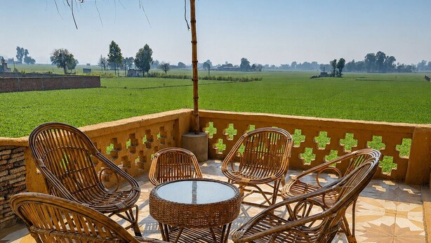 A patio with wicker furniture and a patterned floor, overlooking a green field.