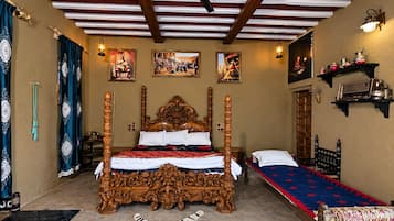 Una cama con dosel tradicional y tallas ornamentales, una cama individual con cubrecama estampado, y una estantería con utensilios de cocina.