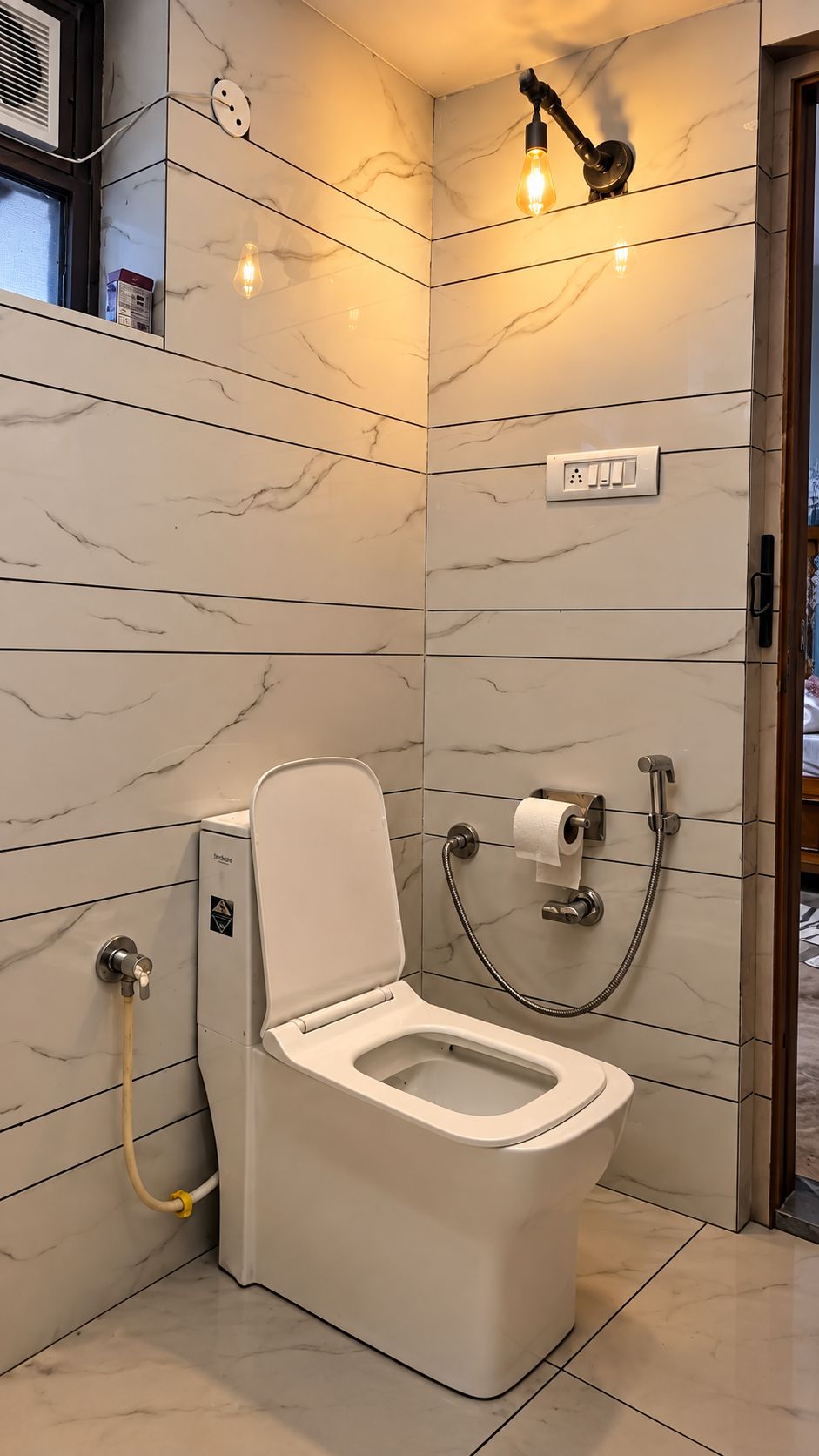 Casa de banho moderna com sanita, chuveiro e candeeiro fixo na parede.