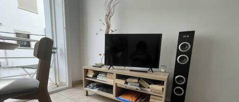 Uma sala de estar com televisão de tela plana, unidade de entretenimento de madeira e uma caixa de som alta.
